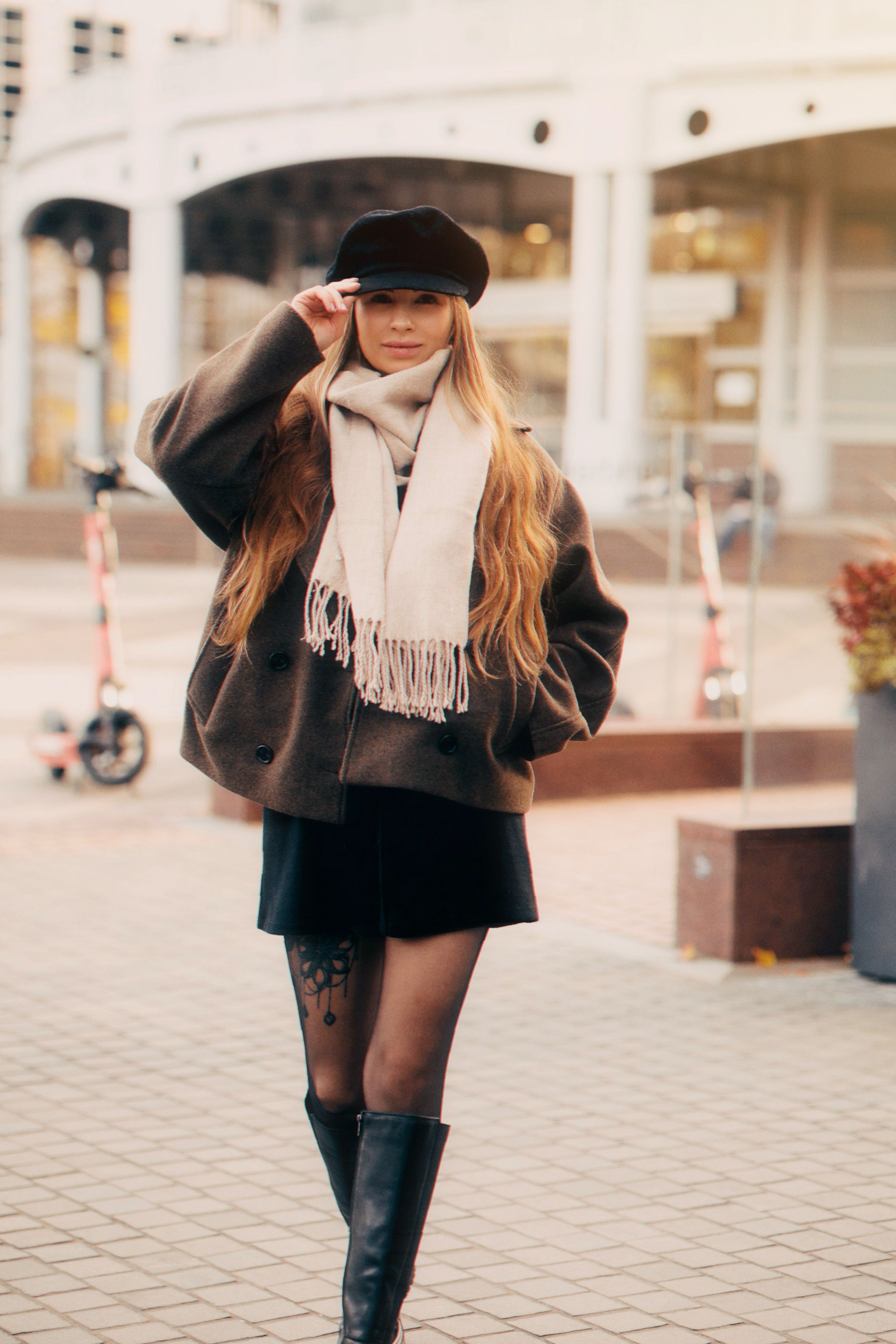 Stylish woman in urban setting wearing a scarf, hat, and boots, perfect for fall fashion inspiration.