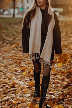 Stylish woman strolls through a park with golden autumn leaves, holding a bouquet.