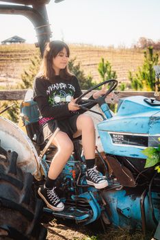 A young woman sits on a vintage tractor in a sunny rural field, enjoying a peaceful day outdoors.
