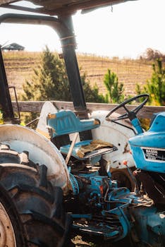 A rustic blue tractor sits idle against a picturesque farmland backdrop, evoking rural charm.