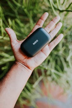 A hand holding a sleek black Rode microphone case against a green background.