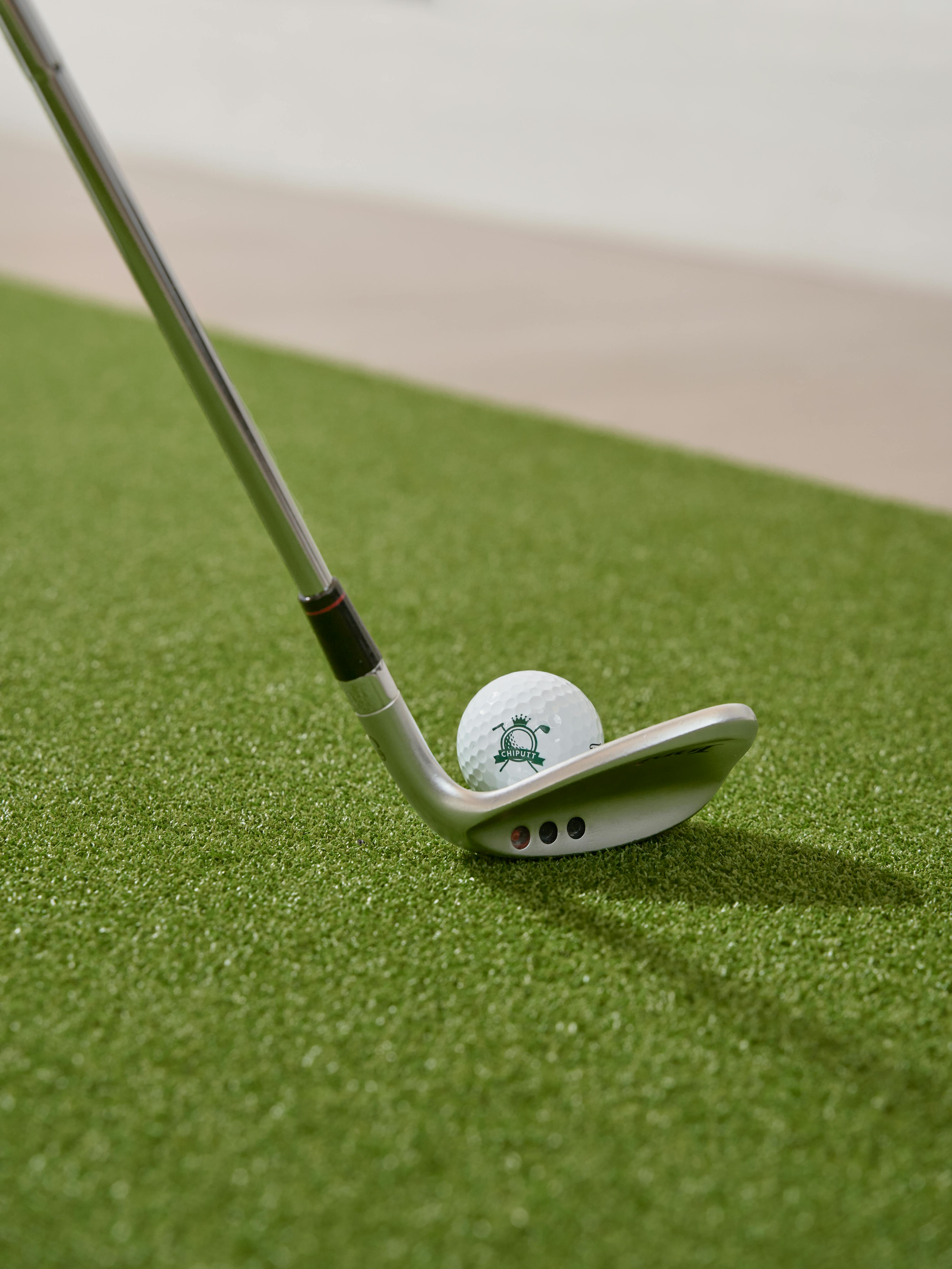 Close-up of a golf club and ball positioned on artificial turf indoors.