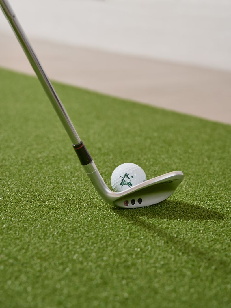 A wedge addressing a golf ball on a hitting mat