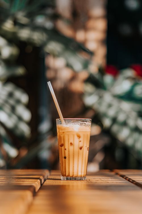 Free A vibrant iced coffee served in a glass with a straw on an outdoor wooden table. Stock Photo