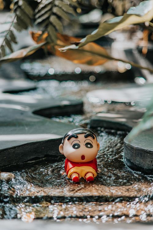 Free Cute figurine on stones amidst flowing water, surrounded by green foliage. Stock Photo
