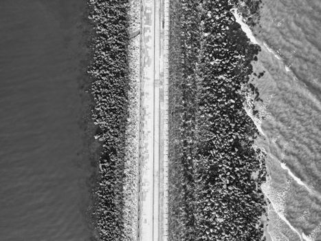 Black and white aerial view of a coastal road flanked by rocks and the sea, showcasing natural contrast.