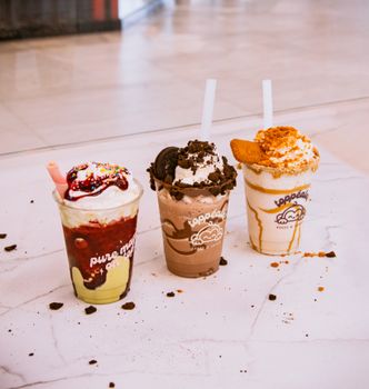 Three colorful milkshakes topped with whipped cream on a marble surface, perfect for dessert inspiration.