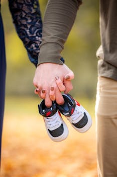 A couple holds a pair of baby shoes symbolizing new beginnings in a beautiful autumn setting.
