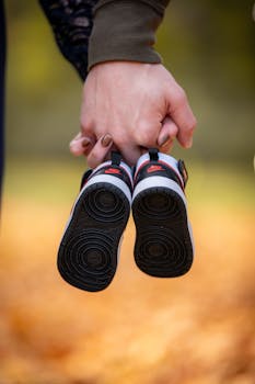 Close-up of baby shoes held by an adult hand in a park setting.