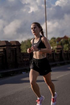 A female runner in athletic wear jogging on a street under a clear sky, embodying fitness and motivation.