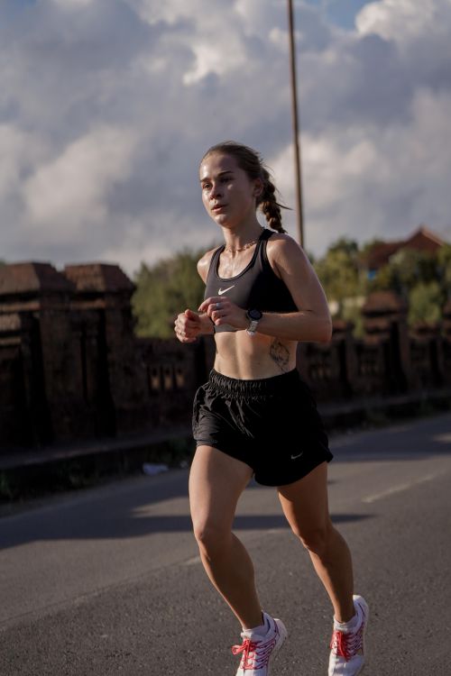 Free A female runner in athletic wear jogging on a street under a clear sky, embodying fitness and motivation. Stock Photo