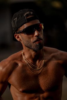 A fit, muscular man wearing sunglasses and a hat enjoys an outdoor workout.