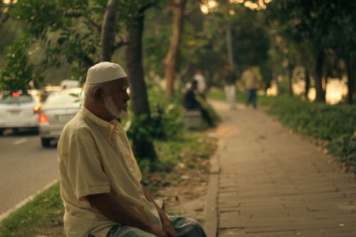 Free An elderly man sitting on a roadside in Dhaka, Bangladesh at dusk. Stock Photo