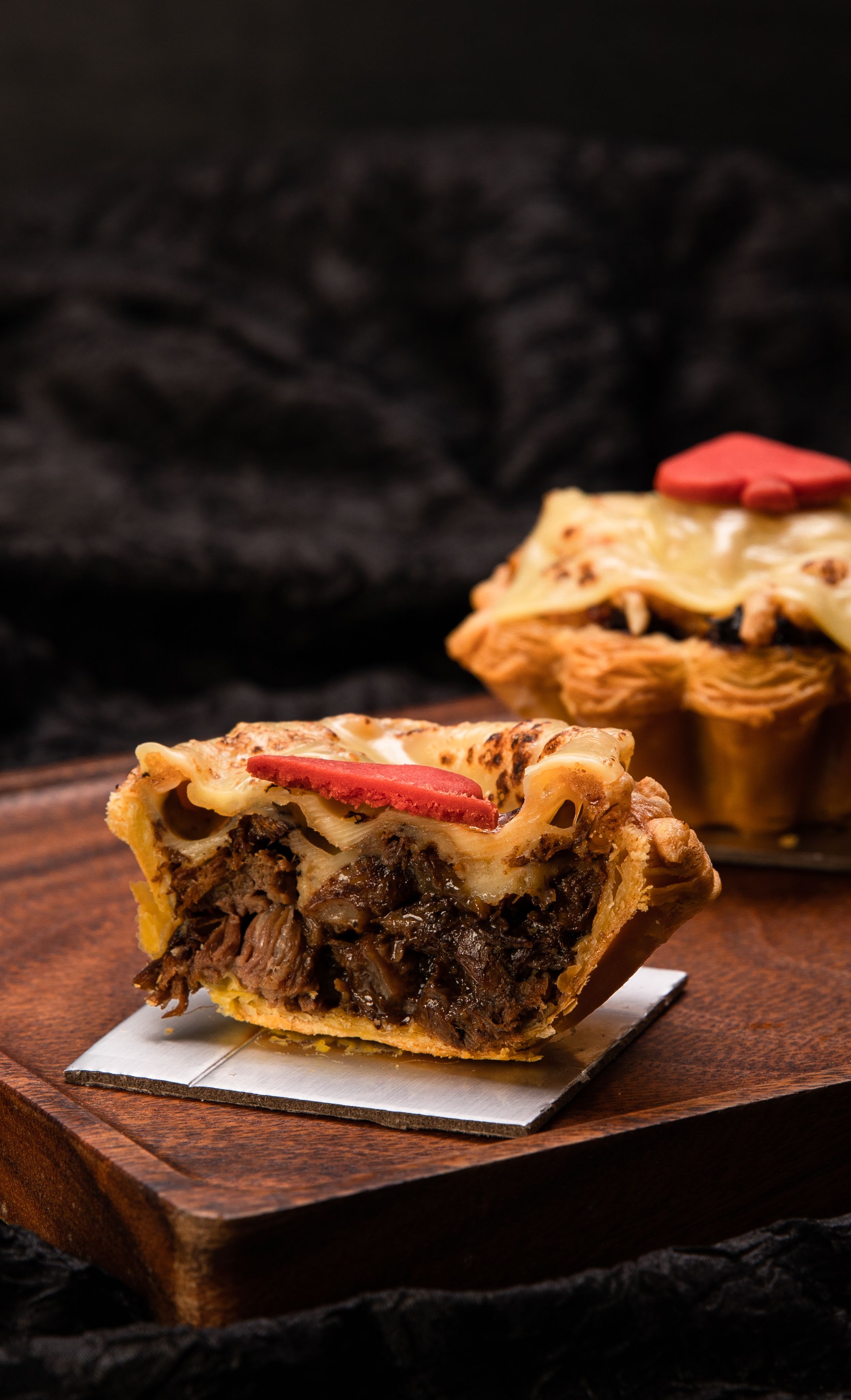 Part de tourte au bœuf effiloché ouverte sur sa garniture, pâte feuilletée et fromage fondu, sur une planche en bois sombre