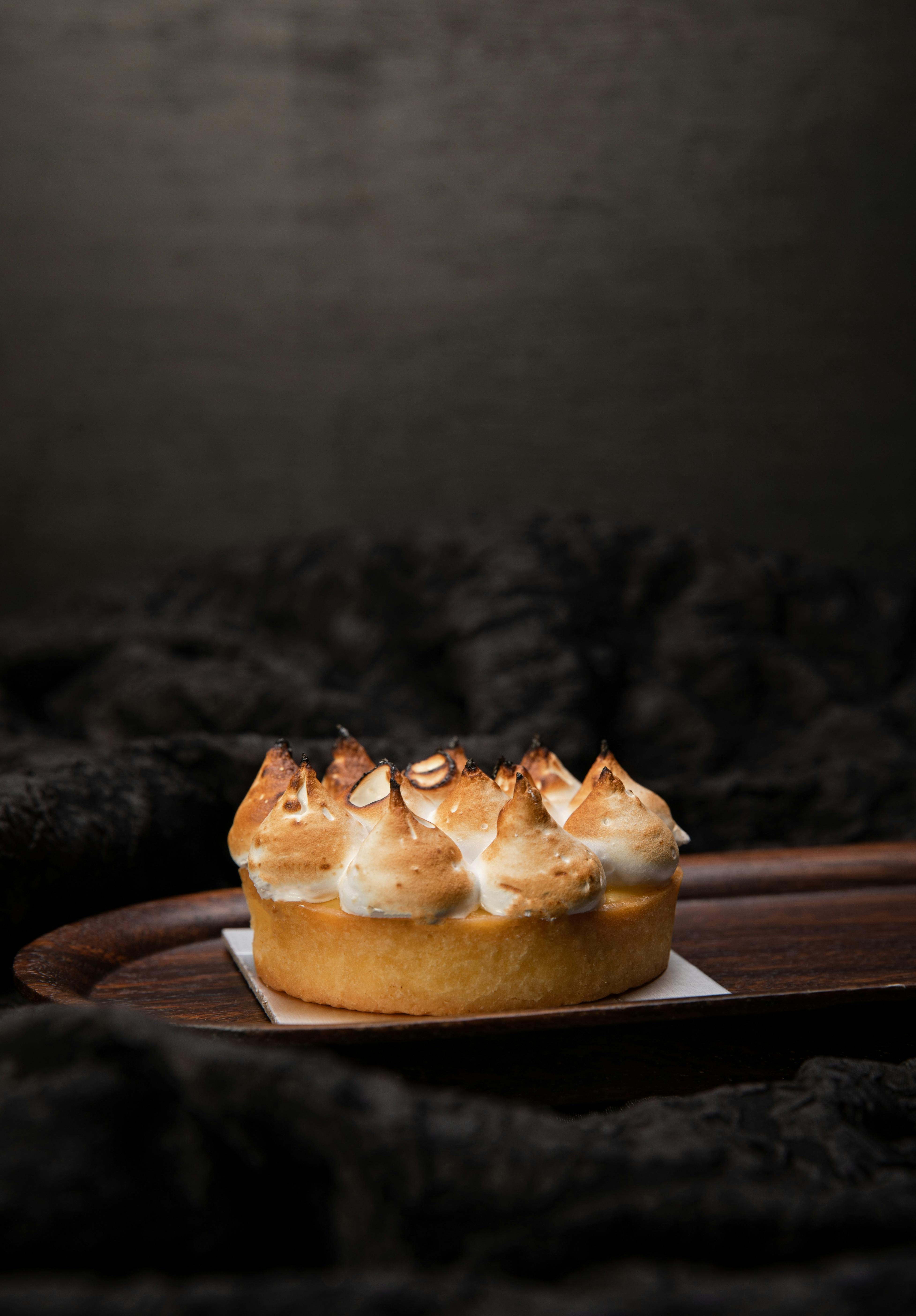 A delicious lemon meringue tart with toasted peaks on a dark wood tray, perfect for gourmet presentations.