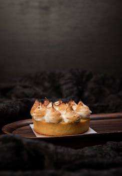 A delicious lemon meringue tart with toasted peaks on a dark wood tray, perfect for gourmet presentations.