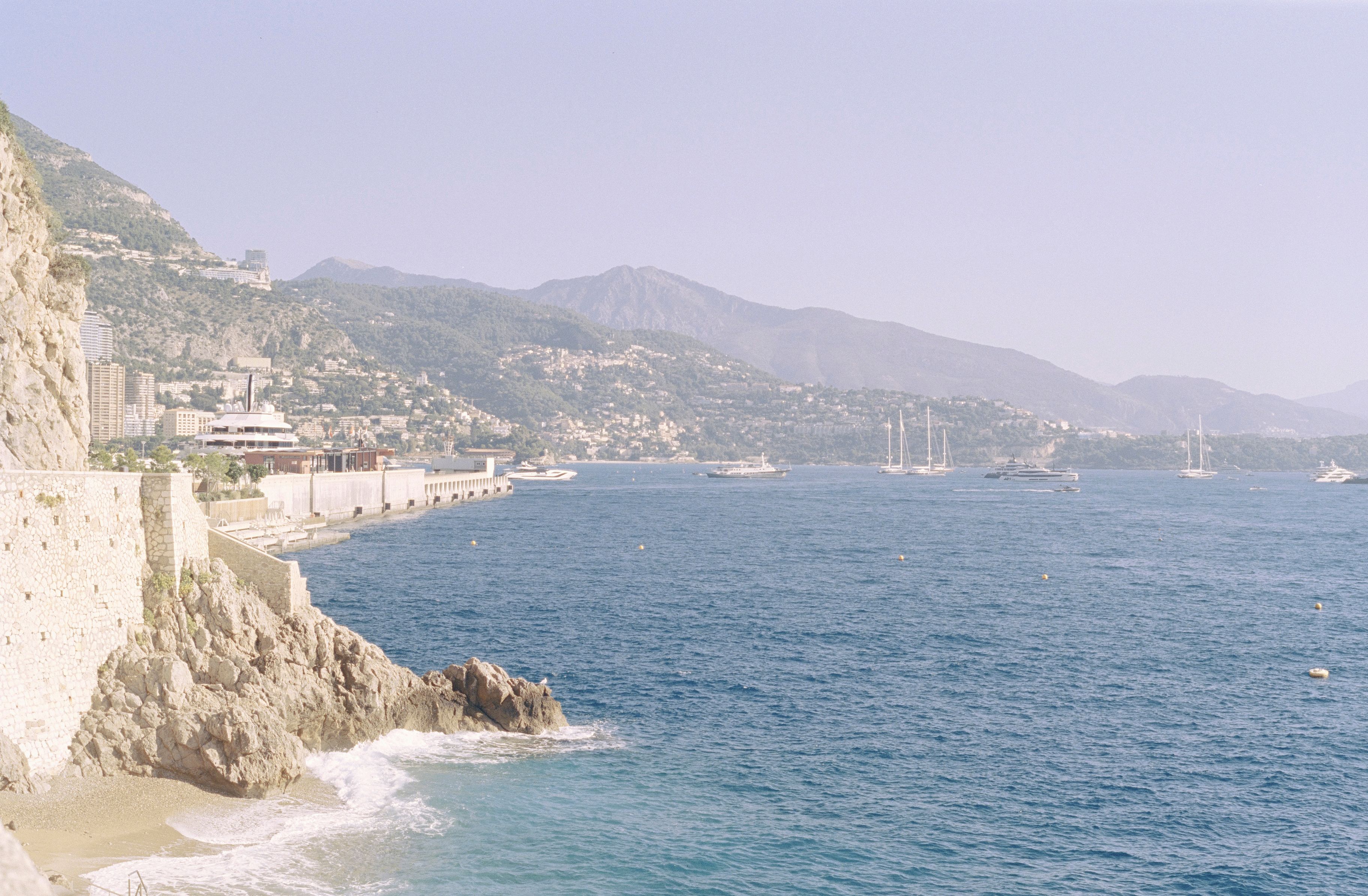 Picturesque view of Monaco coastline with mountains and yachts.