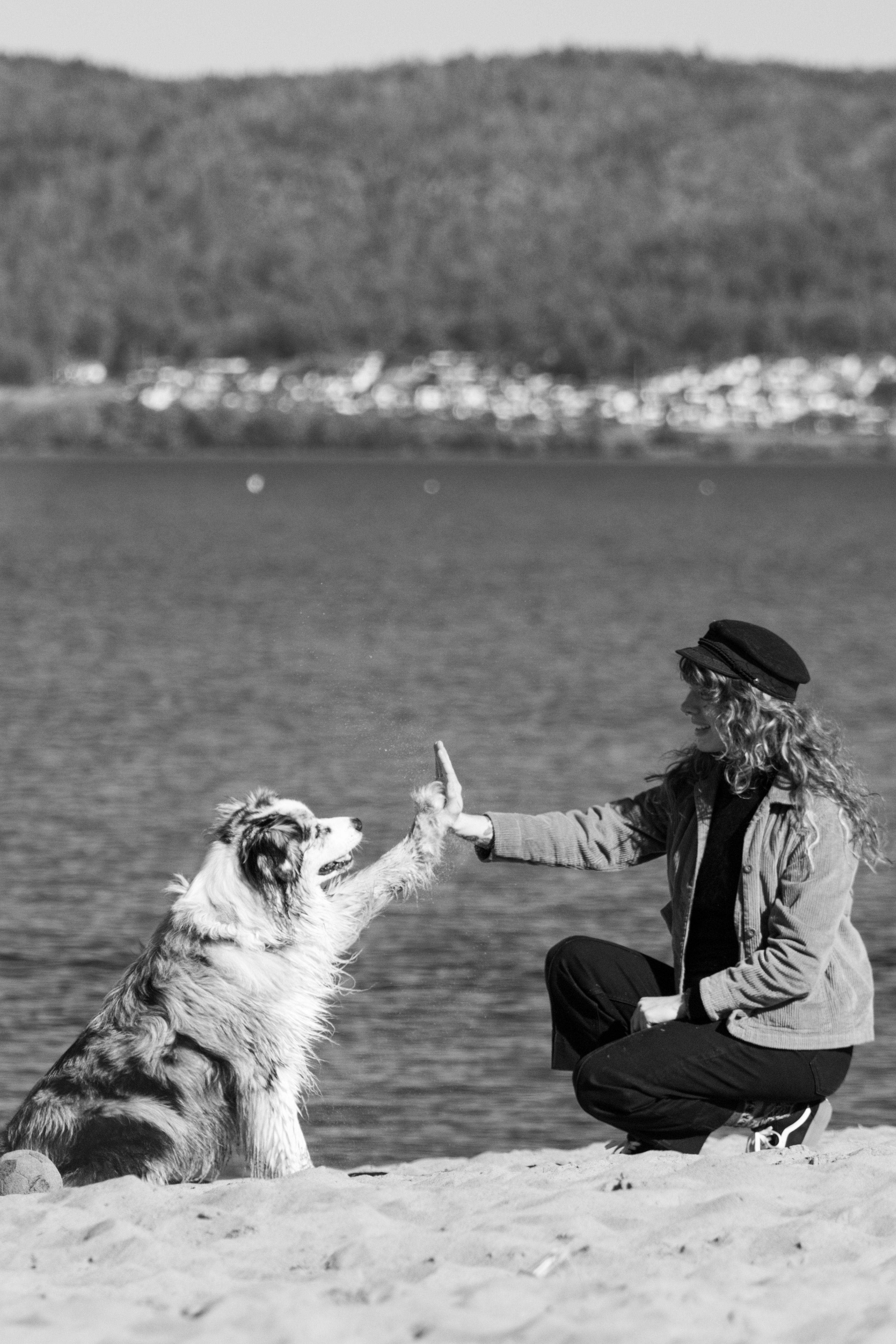Monochrome photo of a woman high-fiving a dog on a Jönköping beach.