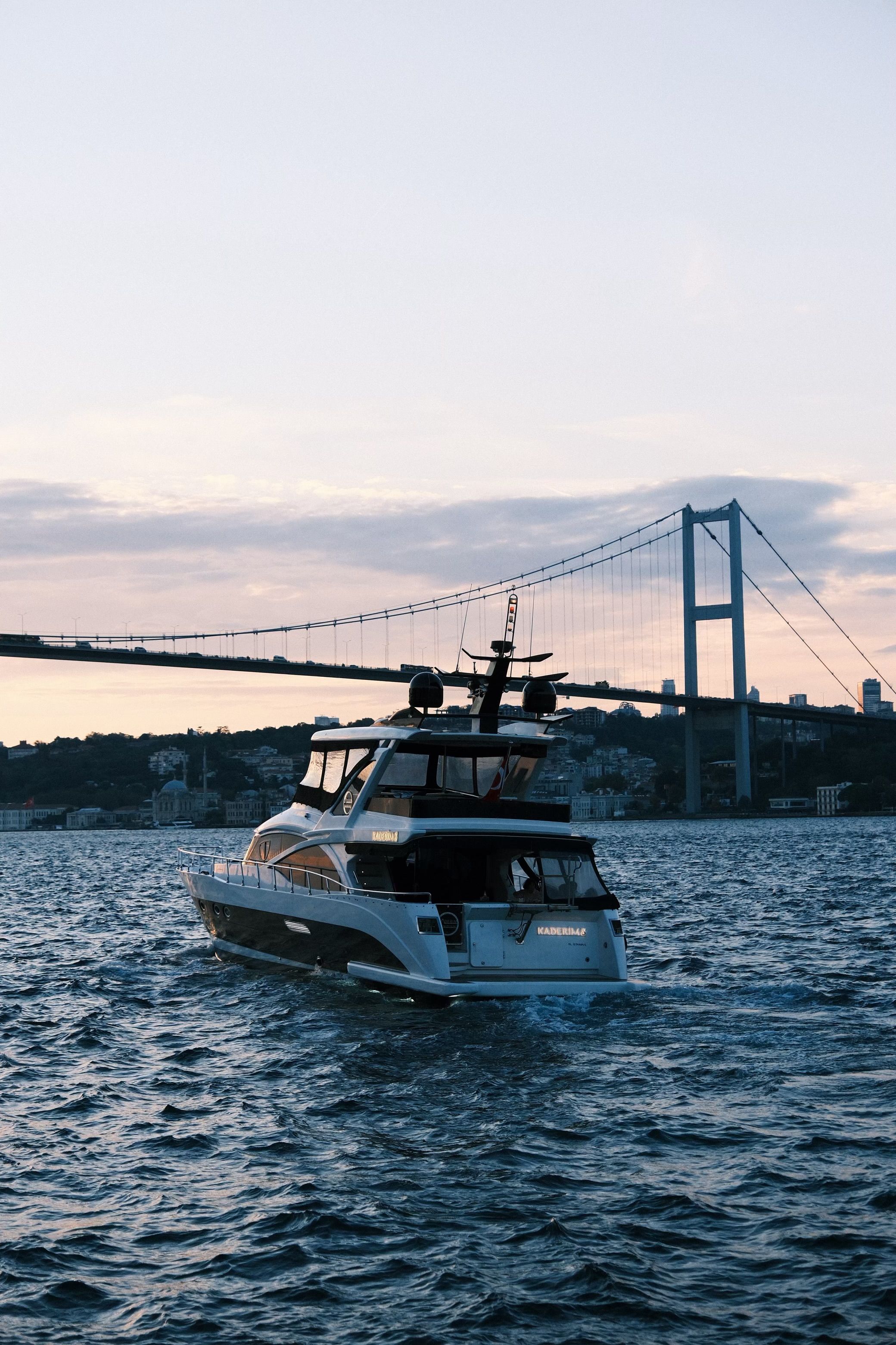 A luxury yacht cruising on the Bosphorus with the Bosporus Bridge in the background at sunset in Istanbul.