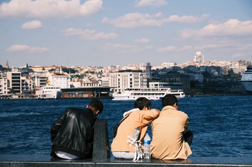 Free Three young adults enjoying a sunny day by the Bosphorus in Istanbul, with a cityscape in the background. Stock Photo