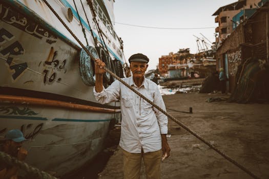 Portrait of an elderly fisherman standing beside a boat in Ras El-Bar, Egypt, showcasing cultural heritage.