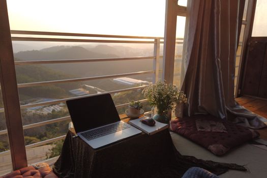 A serene workspace with a laptop and flowers overlooking Dalat's picturesque hills at sunset.