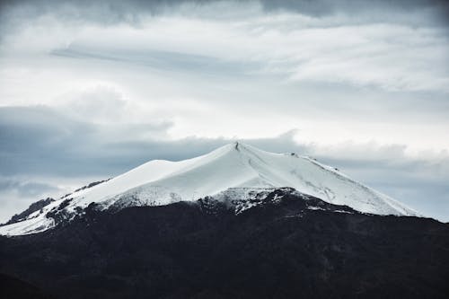 Majestic mountain range with snow covered summit against gloomy overcast sky in winter highlands