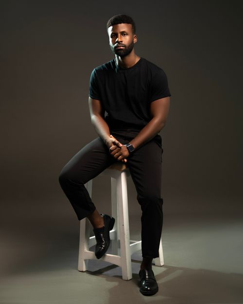 Free Stylish portrait of a man sitting on a stool in a studio setting, wearing a black outfit. Stock Photo