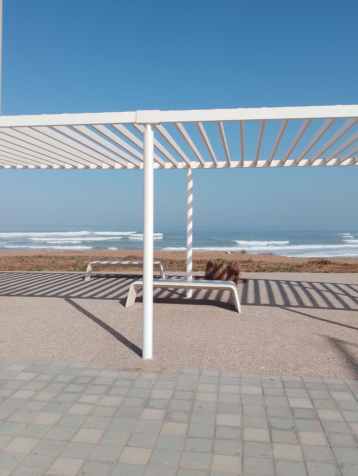 Weißes Lamellendach mit geöffneten Lamellen gegen blauen Himmel am Meer
