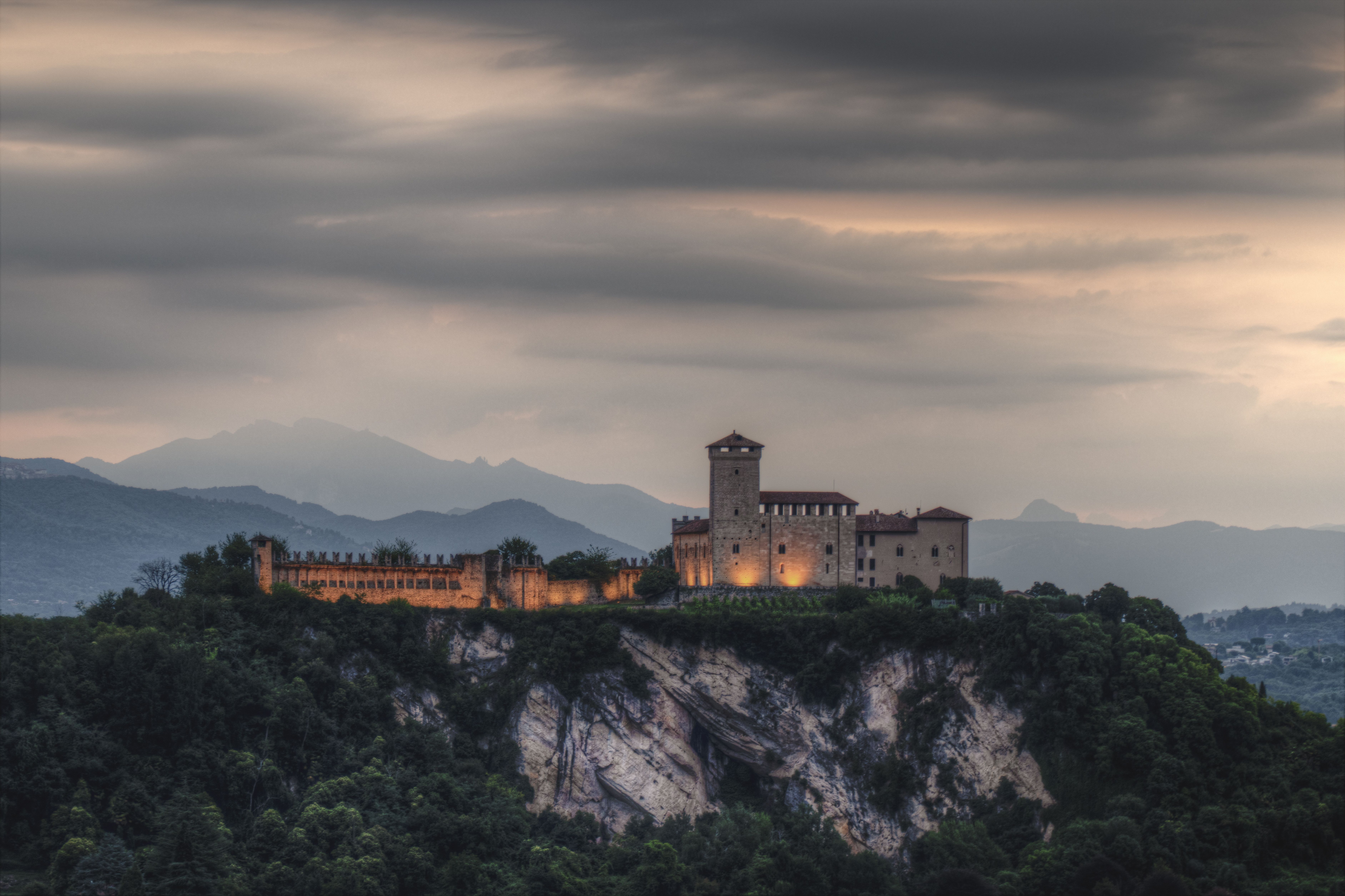A stunning view of an illuminated castle perched on a rocky cliff under a moody sky.