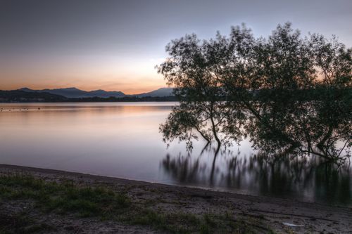 Free Tranquil sunset over a calm lake with tree reflections and distant mountains. Stock Photo