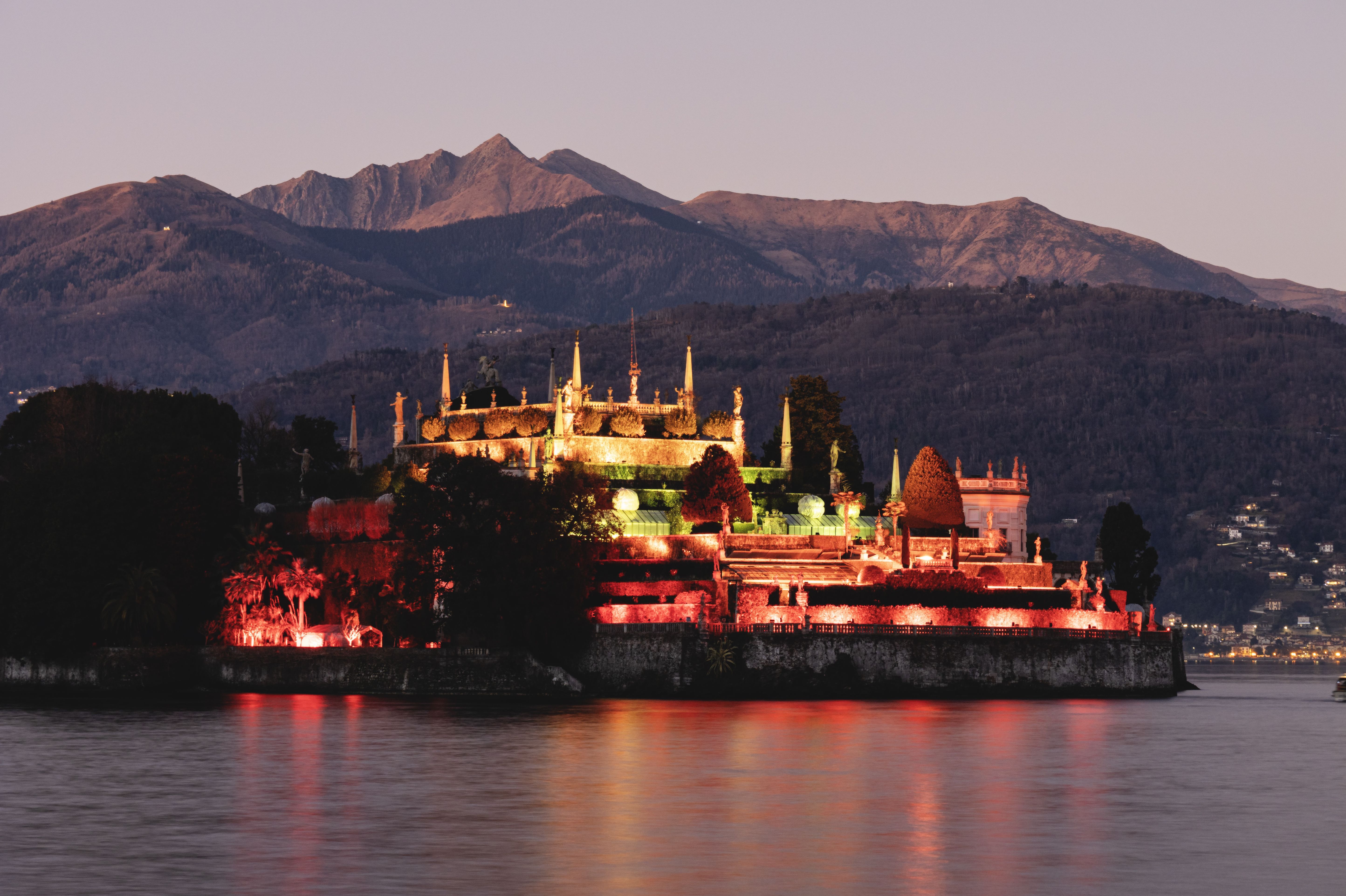 Illuminated Isola Bella at dusk with picturesque mountains in background. Illuminated Isola Bella at dusk with picturesque mountains in background.