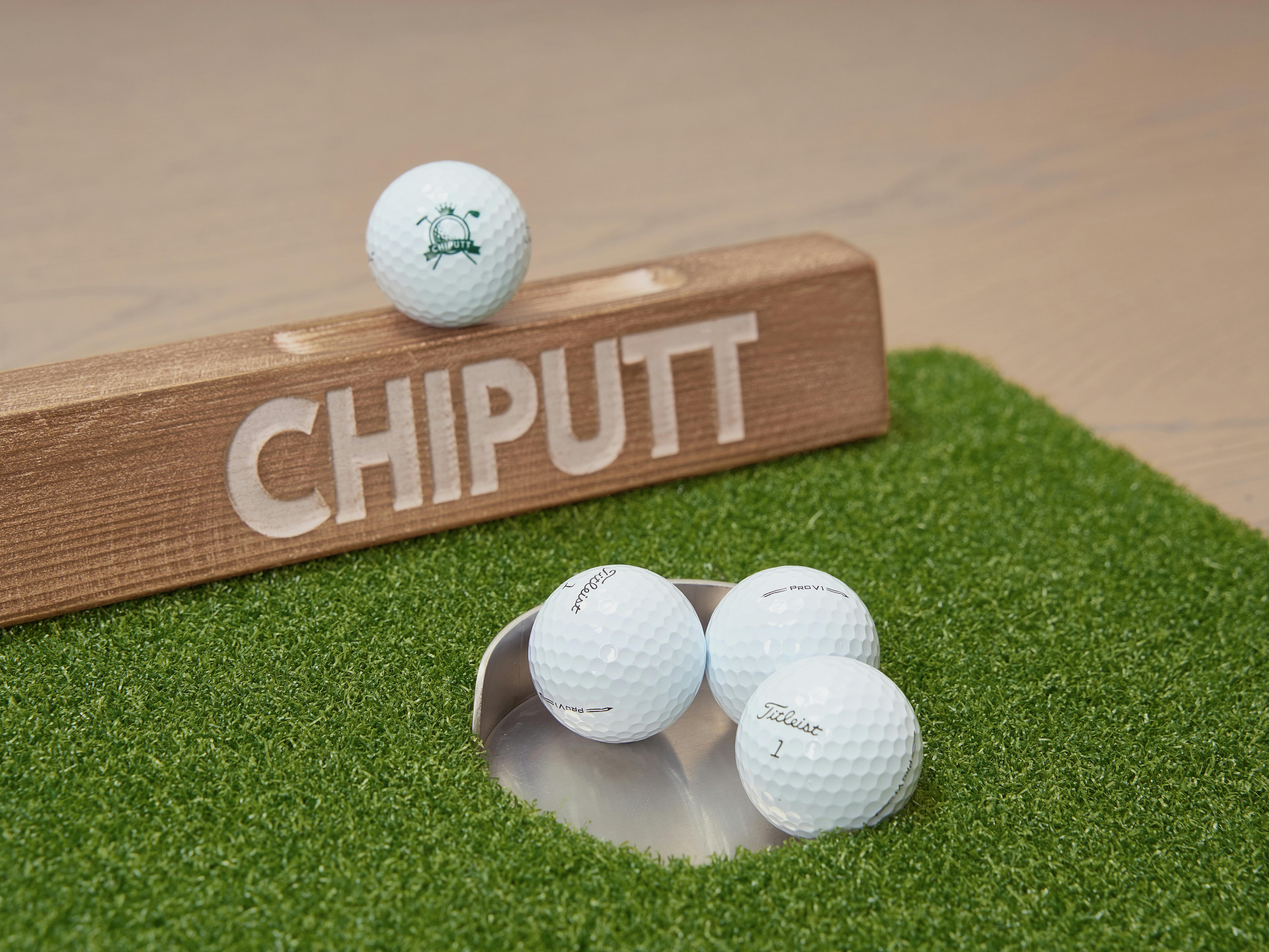 Wooden chipping putt board with golf balls on artificial green mat for training.