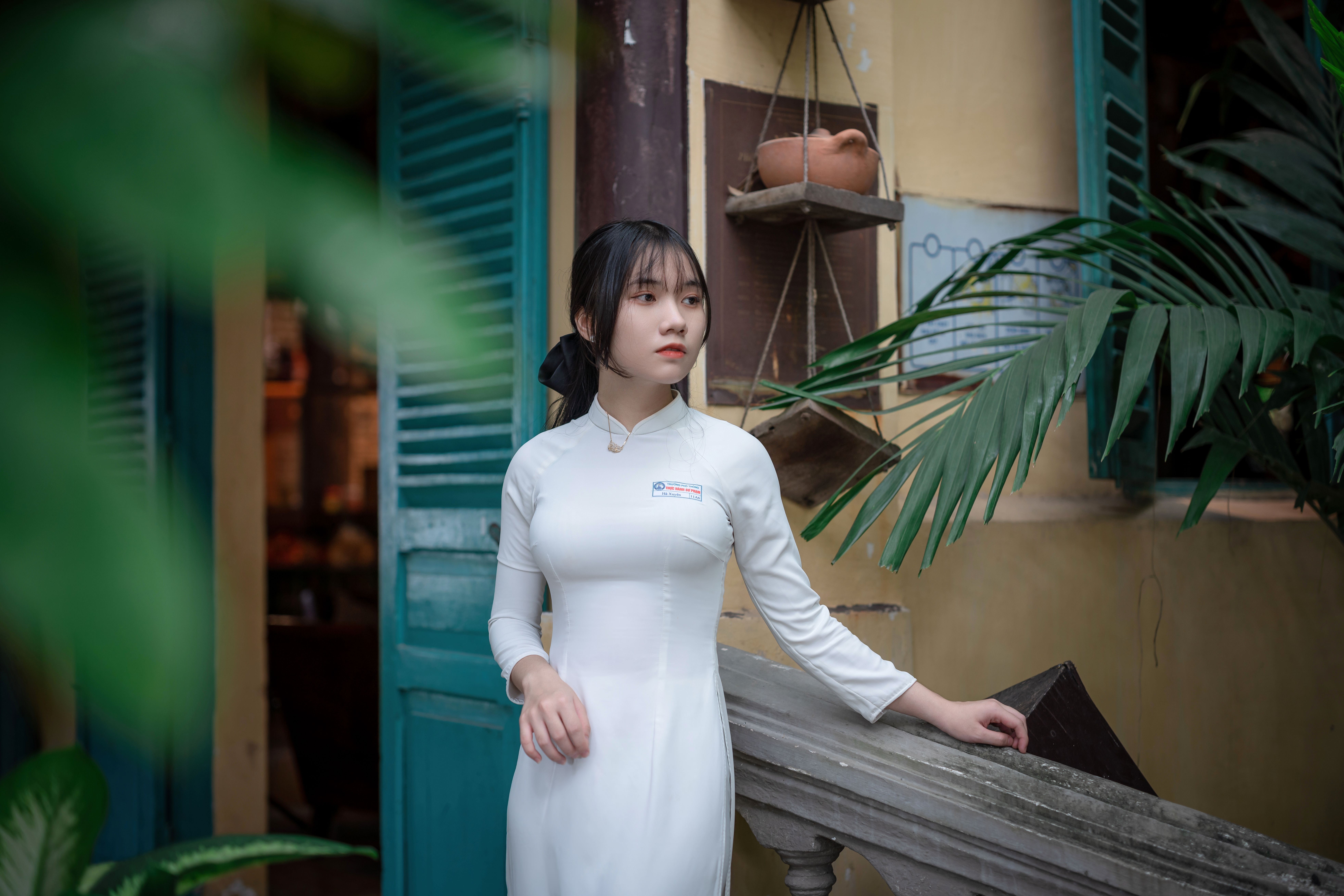 Portrait of a young woman in white ao dai, standing in a traditional Asian setting.