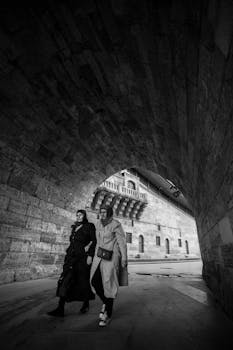 Two women walking under a stone archway in İstanbul, Türkiye, in black and white.