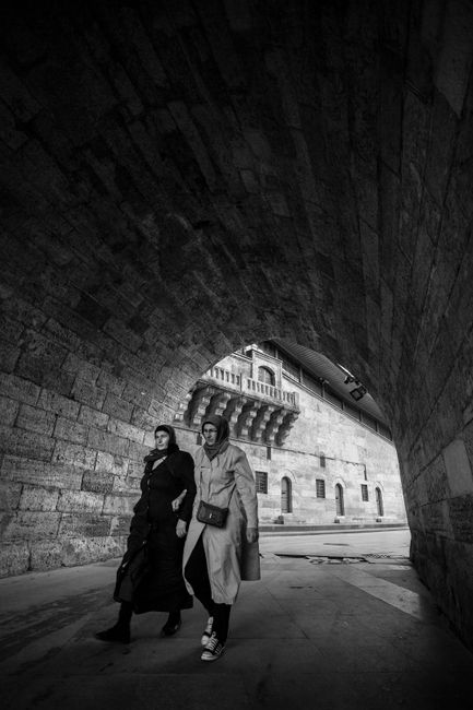 Two women walking under a stone archway in İstanbul, Türkiye, in black and white.