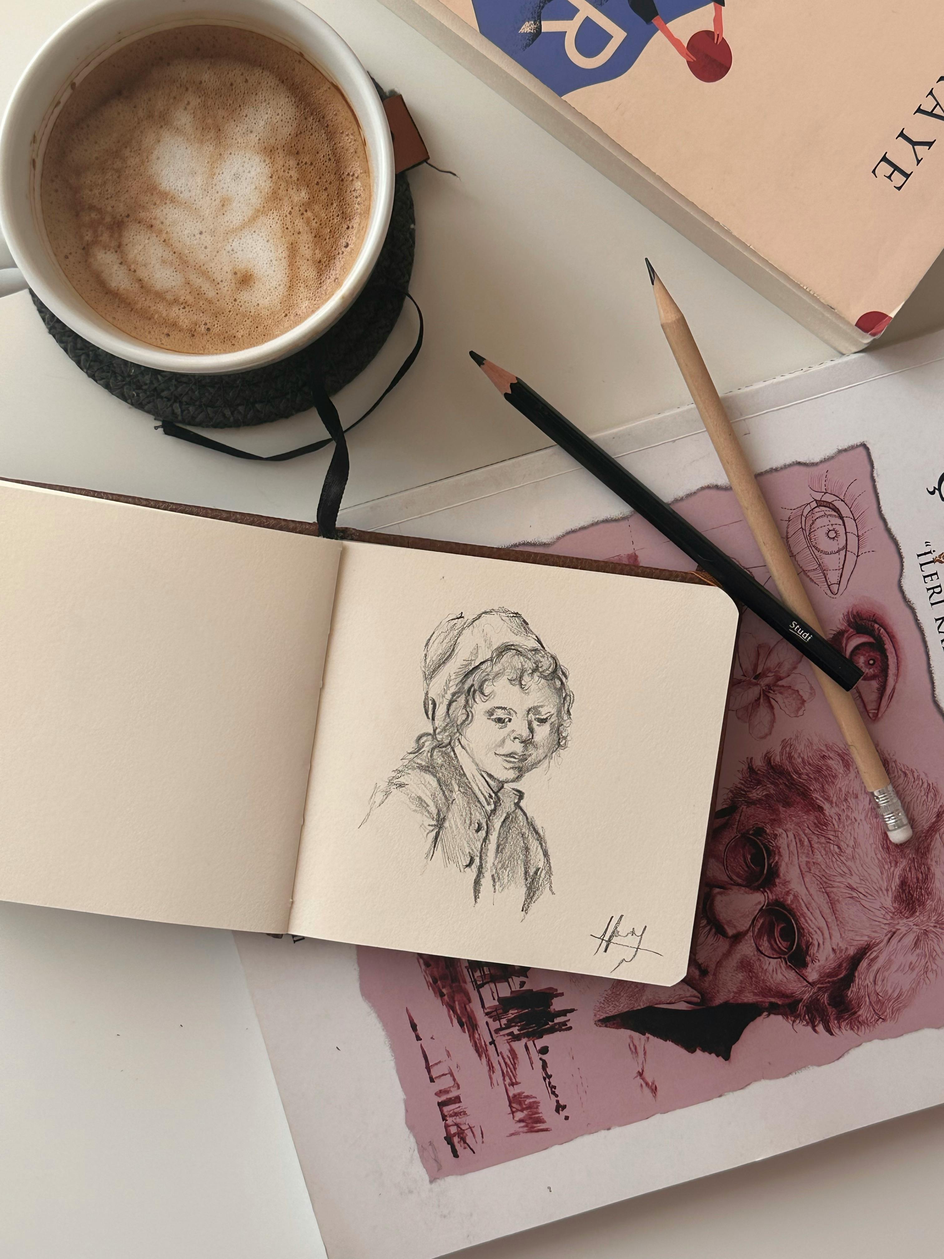 Cozy artist's workspace featuring a sketchbook, coffee, and art supplies.