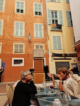 Two women enjoy conversation at a quaint outdoor café in Nice, surrounded by historic architecture.