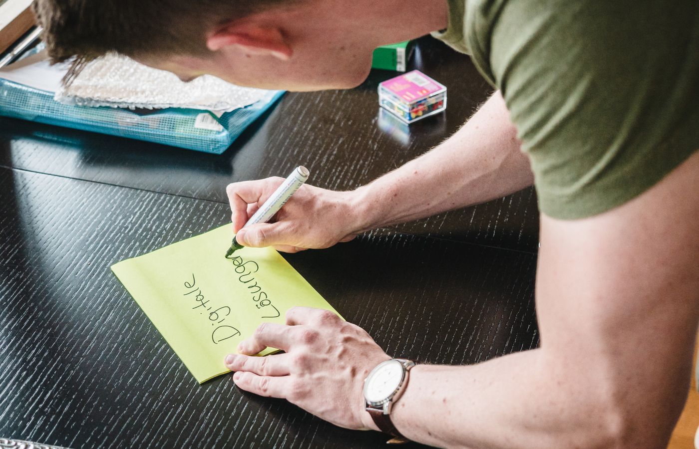 Man writes digital solutions on a note at a desk indoors, showcasing creativity.