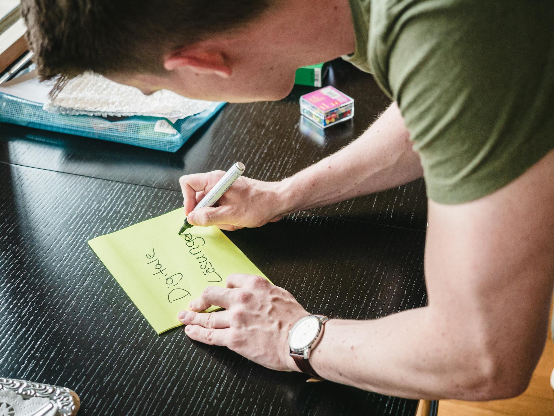 Man writes digital solutions on a note at a desk indoors, showcasing creativity.