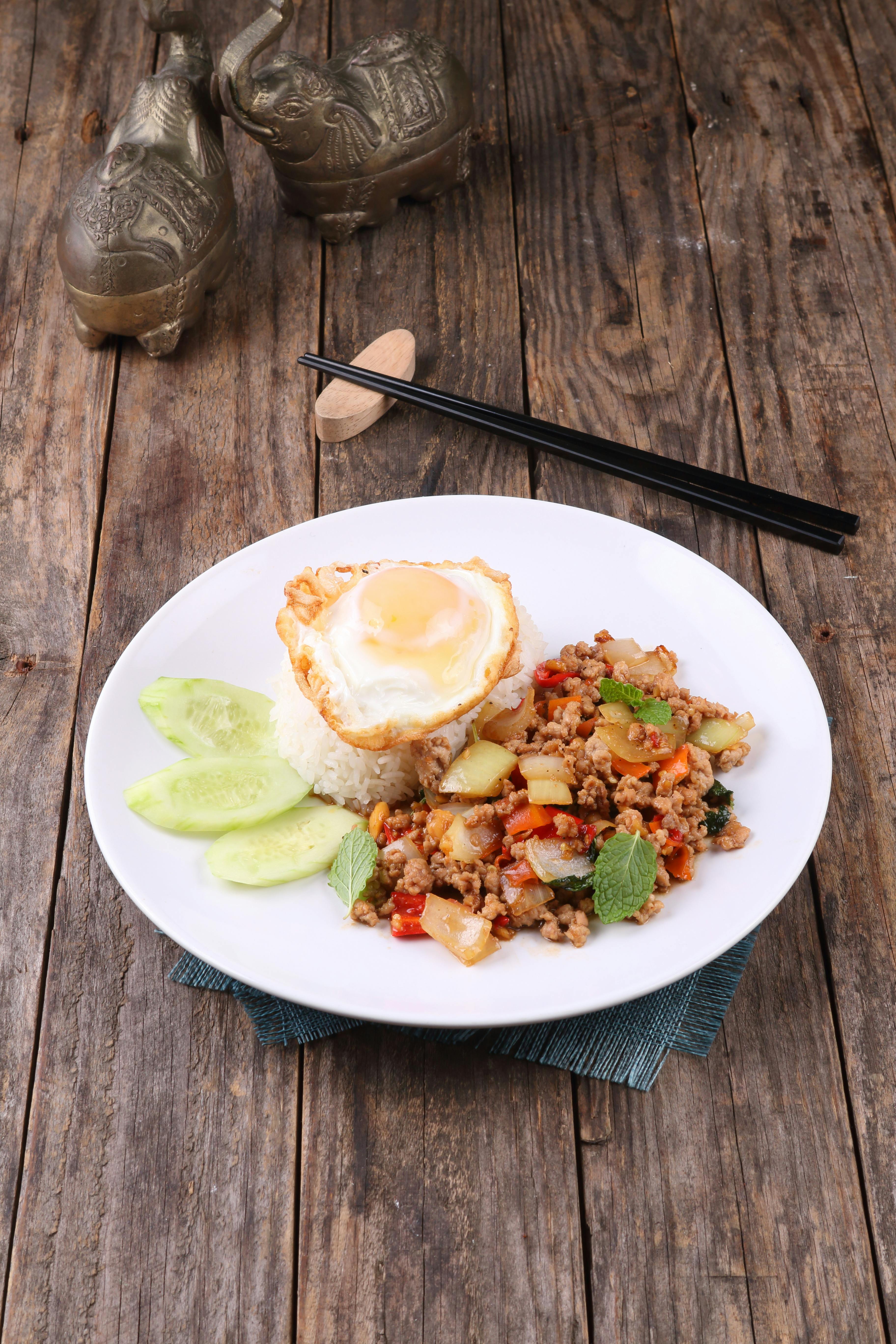 Bowl of spicy Thai ground pork stir-fry topped with a fried egg, served over jasmine rice with wilted basil visible throughout