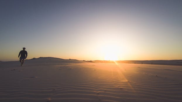 Silhouette of a man walking across sand dunes during sunset in Ghan, Australia.