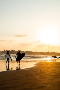 Surfers carrying boards along Weligama Beach in Sri Lanka during a warm sunset.
