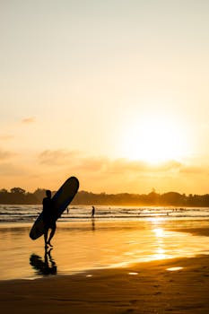 Silhouette of a surfer walking along Weligama Beach at sunset, capturing the serene ocean waves.
