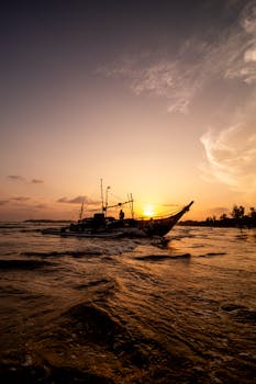 Fishermen sail a traditional boat at sunset on Weligama Bay, Sri Lanka.