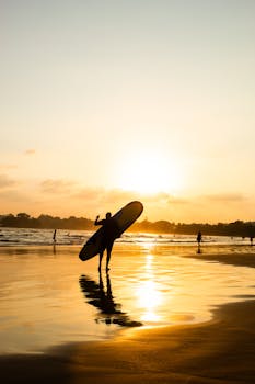 A silhouette of a surfer carrying a board at sunset on Weligama beach, Sri Lanka.