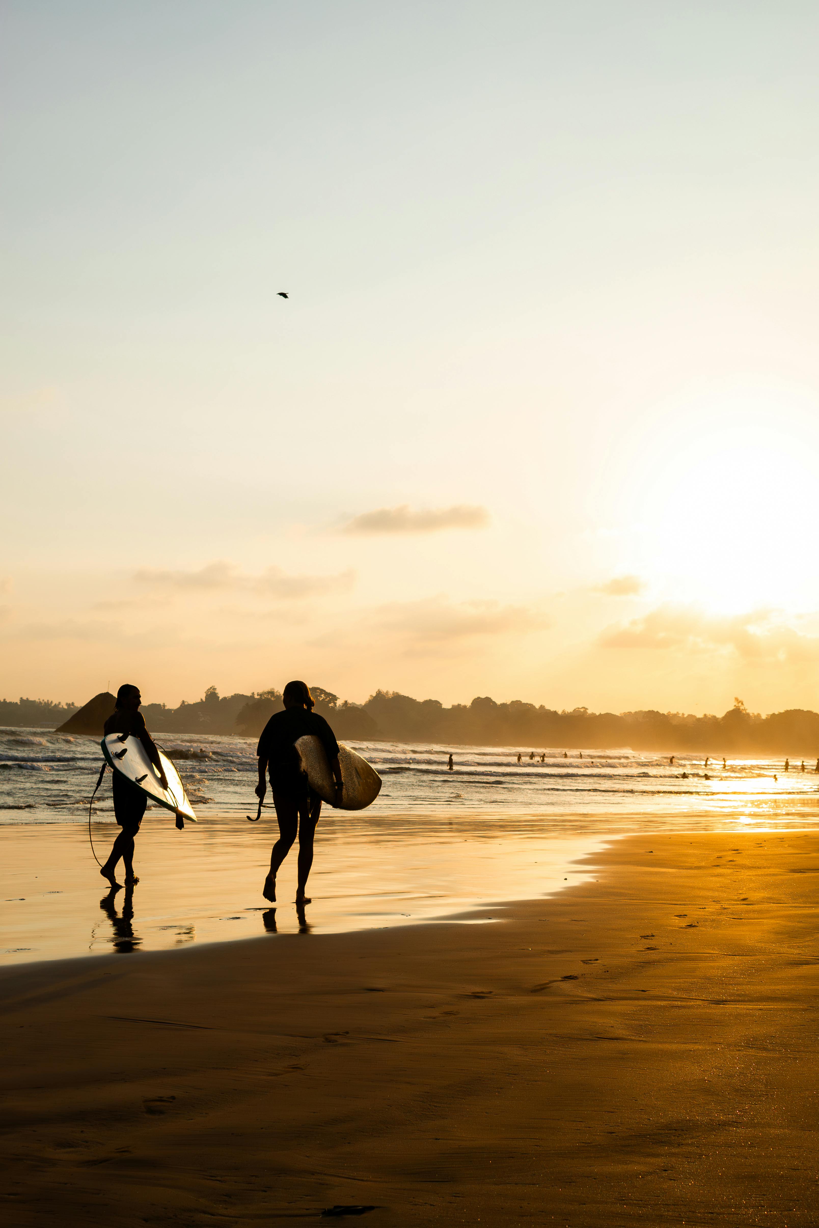 Two surfers walk along Weligama Beach at sunset, capturing the essence of Sri Lankan surfing culture.