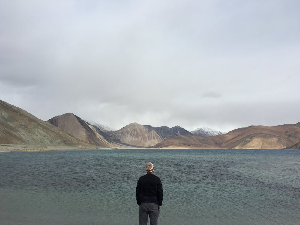 бесплатная Человек, стоящий перед водоемом с холмами на расстоянии Стоковое фото