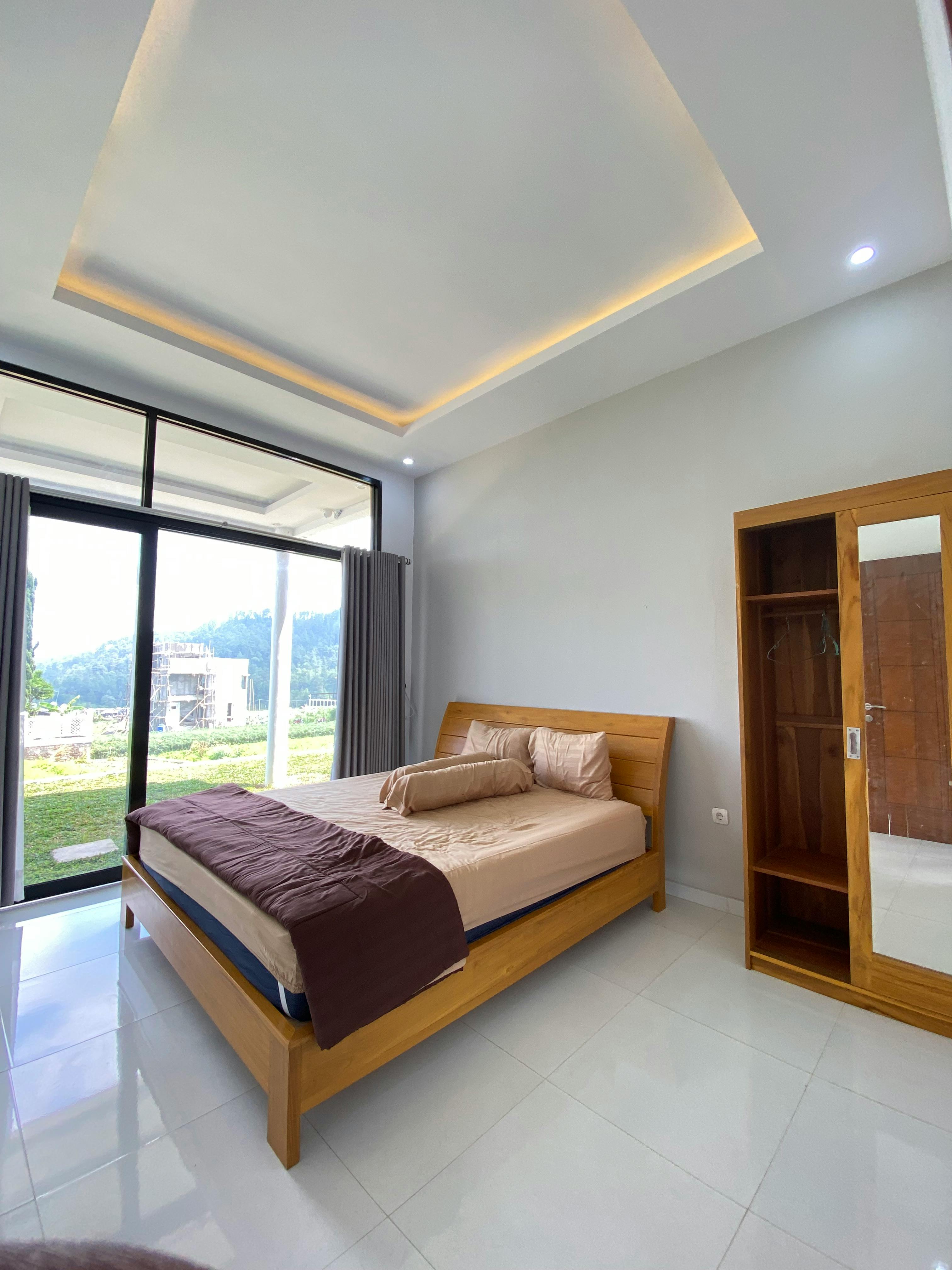 Spacious modern bedroom featuring wooden furniture and large windows overlooking nature.