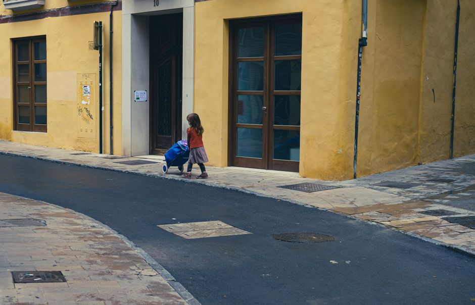 Una niña pequeña tira de un carrito por la esquina de una calle de la ciudad con paredes amarillas.